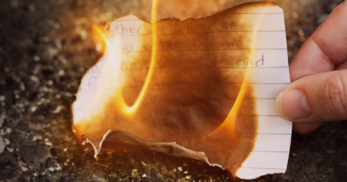 Fingers holding a burning page with handwritten text—symbolizing writing goals for May and letting go of what no longer serves your story.