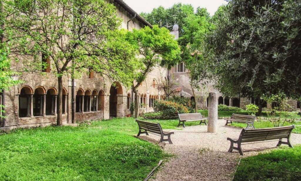 Medieval cloister garden of San Cosimato in Trastevere, Rome, with benches beneath green trees and arched brick walkways.